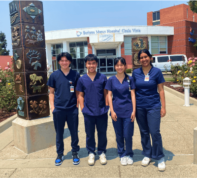 A diverse cohort of students in hospital scrubs posing in front of a Scripps hospital