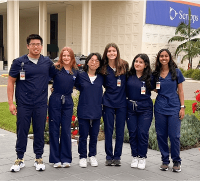 A diverse cohort of students in hospital scrubs posing in front of a Scripps hospital