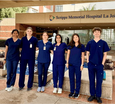 A diverse cohort of students in hospital scrubs posing in front of a Scripps hospital
