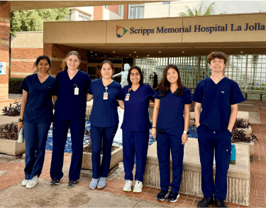 A diverse cohort of students in hospital scrubs posing in front of a Scripps hospital