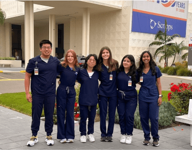 A diverse cohort of students in hospital scrubs posing in front of a Scripps hospital