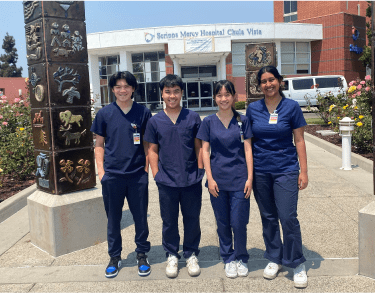 A diverse cohort of students in hospital scrubs posing in front of a Scripps hospital