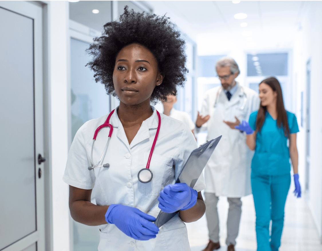 A female nurse walking down a hospital hallway holding a clipboard