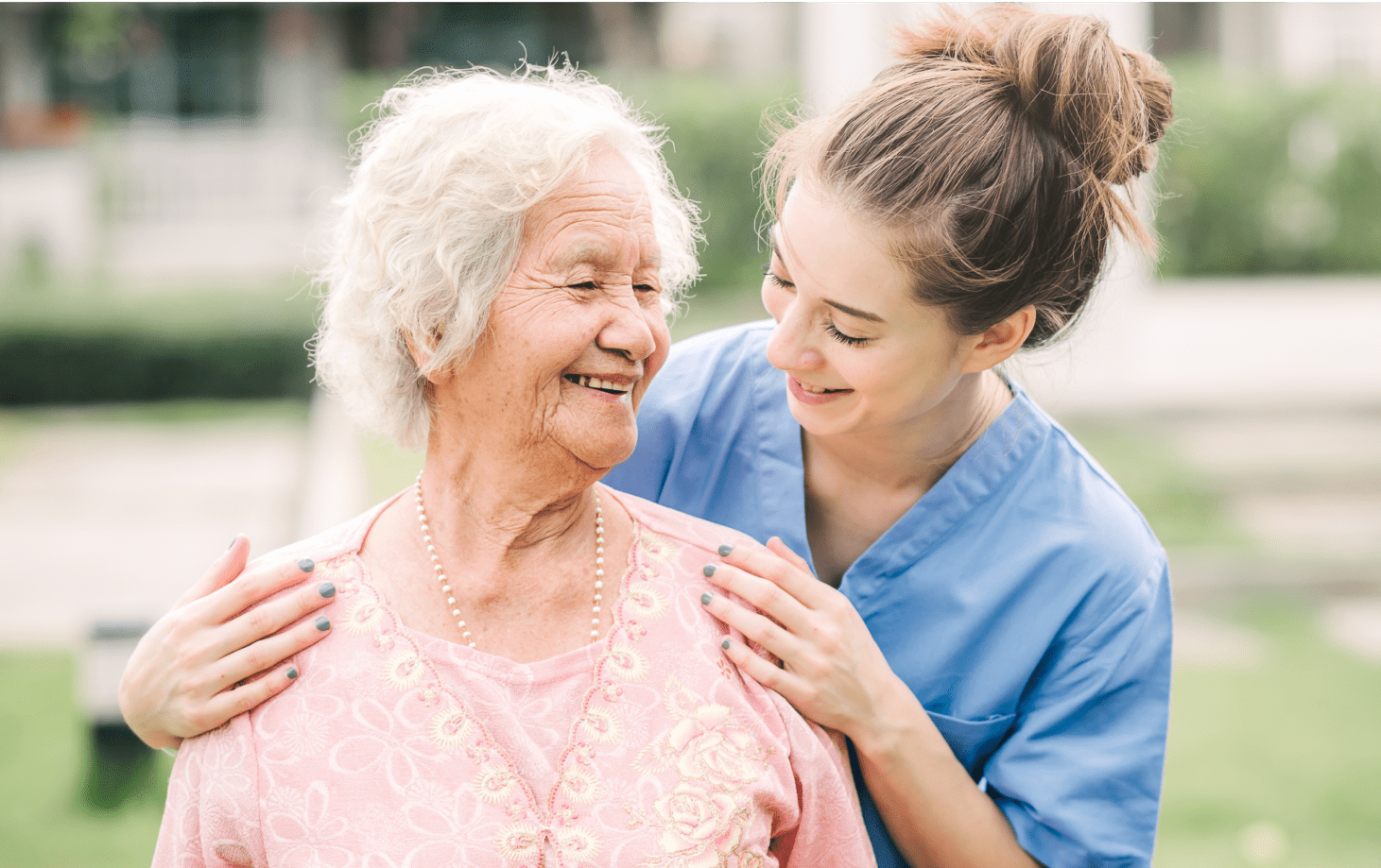 Rectangle 116 (5) A smiling female nurse putting her hands on the shoulders of an elderly female patient