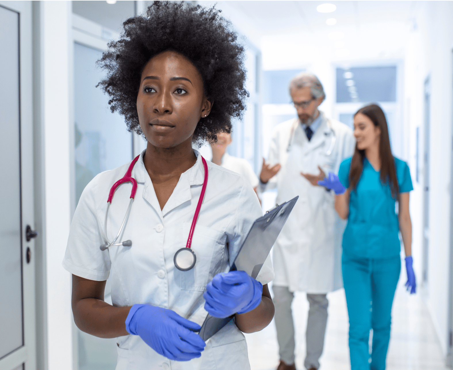 A female nurse walking down a hospital hallway holding a clipboard